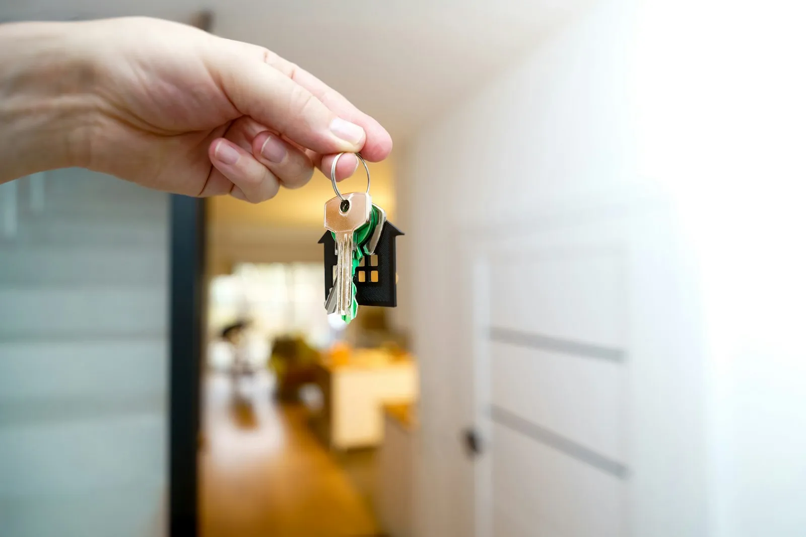 Hand hält Wohnungsschlüssel mit Haus-Anhänger vor einer Wohnungstür